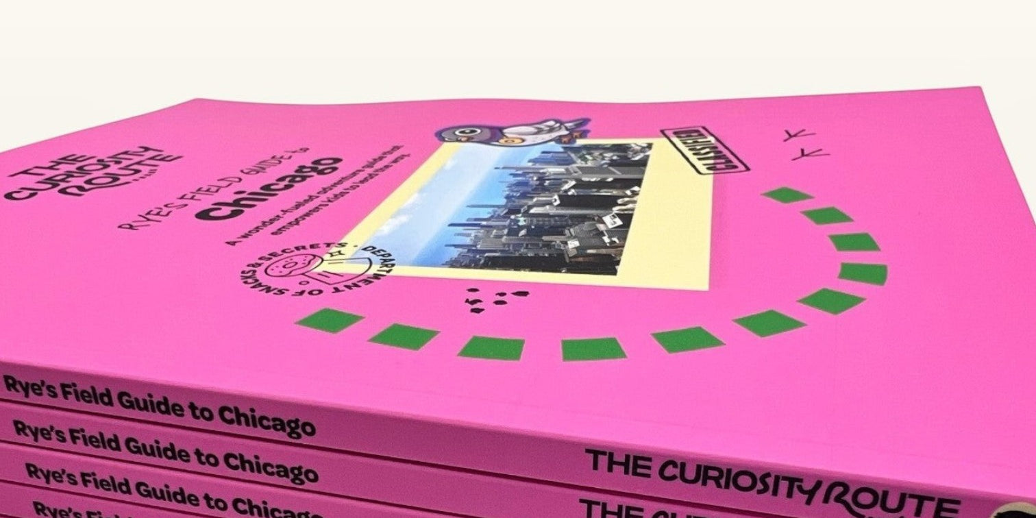 A stack of The Curiosity Route Rye's Field Guide to Chicago books with bright pink covers and illustrated pigeon mascot.