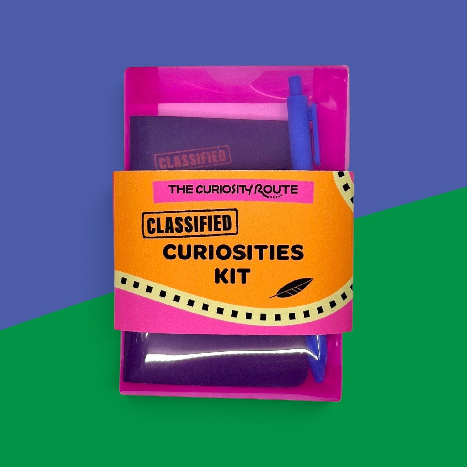 The Curiosity Route Classified Curiosities Kit in a pink envelope with a blue pen and secret message supplies.