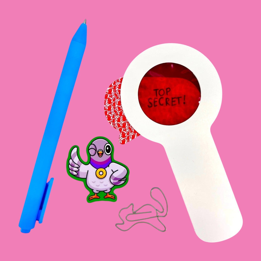 The Curiosity Route Classified Curiosities Kit featuring a blue pen, red decoder lens, pigeon sticker, and squirrel-shaped paperclip.