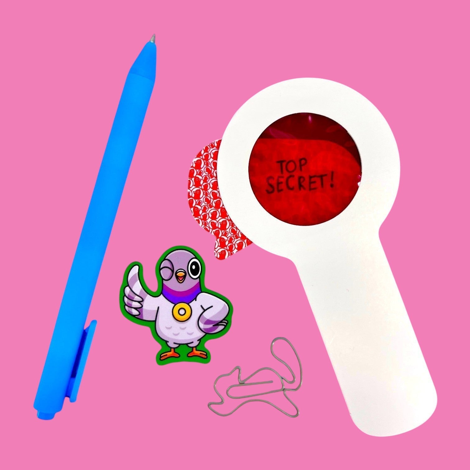 The Curiosity Route Classified Curiosities Kit featuring a blue pen, red decoder lens, pigeon sticker, and squirrel-shaped paperclip.
