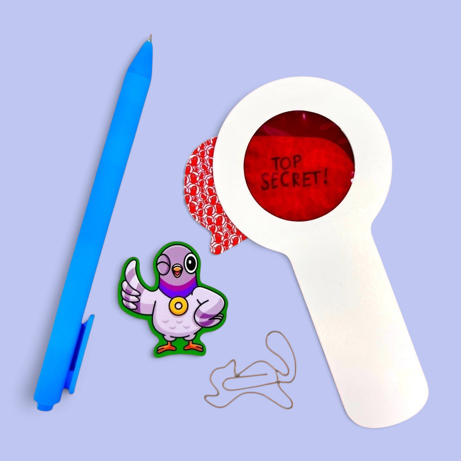 The Curiosity Route Classified Curiosities Kit featuring a blue pen, red decoder lens, pigeon sticker, and squirrel-shaped paperclip.