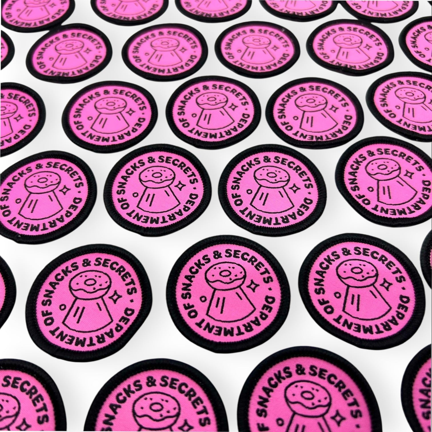 The Curiosity Route circular pink embroidered patch with Department of Snacks and Secrets text and donut icon