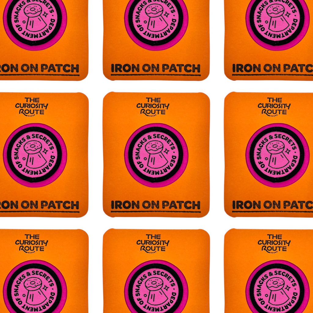 The Curiosity Route circular pink embroidered patch featuring a donut icon and Department of Snacks and Secrets text.