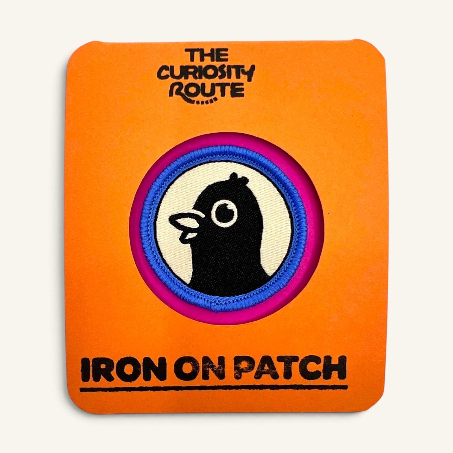 The Curiosity Route Top Pigeon woven iron-on patch featuring a black pigeon illustration on a bright orange backing.
